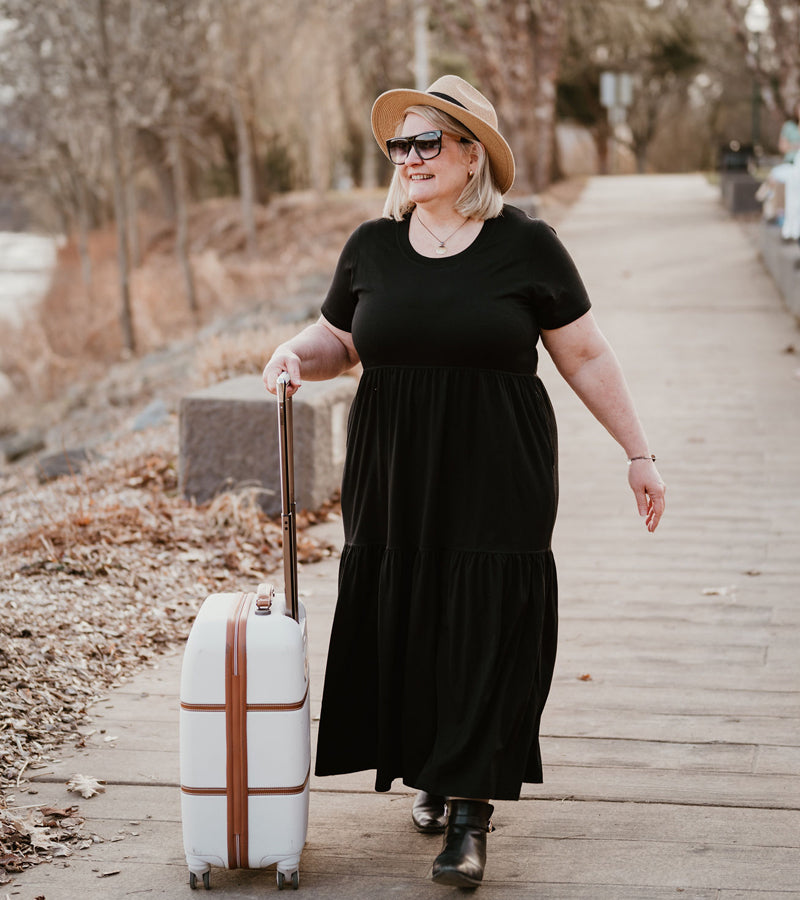Model wearing black Lucia dress and rolling a suitcase