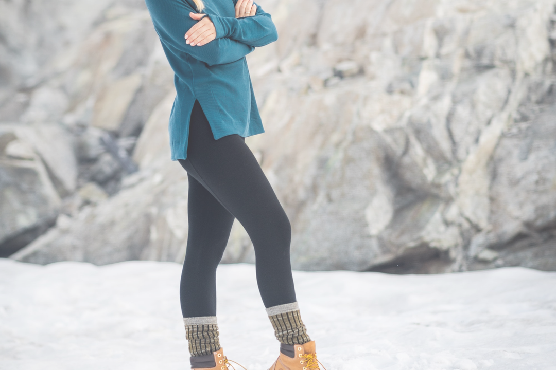 girl standing outside on snow with rocks behind her wearing black leggings and green top. 
