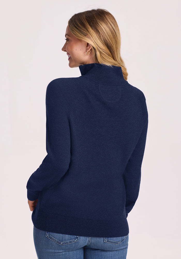 A woman in the Woolx Collins Half Zip Sweater in Ocean Cavern stands smiling over her shoulder, back turned.