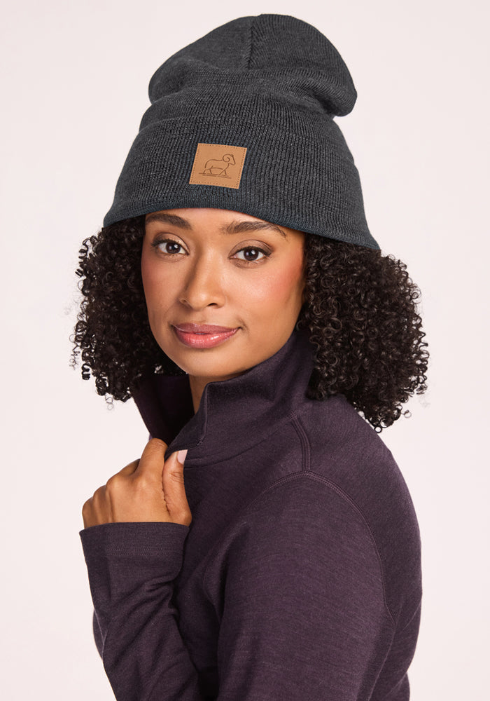 Woman with curly hair wears a Woolx Baylor Beanie in Cinder Melange and a purple zip-up, smiling at the camera.