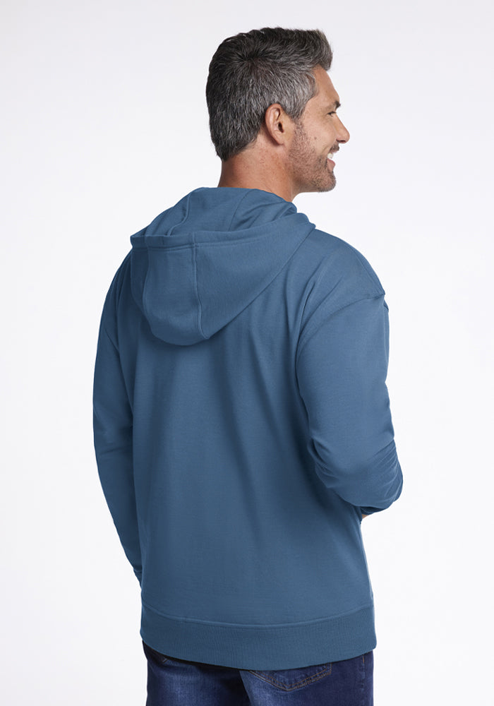Man with short gray hair in Woolx Chase Hoodie - Blue Ashes and jeans, smiling against a plain background.