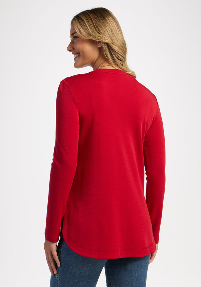 Woman in Woolx Blair Tunic - Maraschino Cherry and jeans, standing and smiling, seen from the back on white.