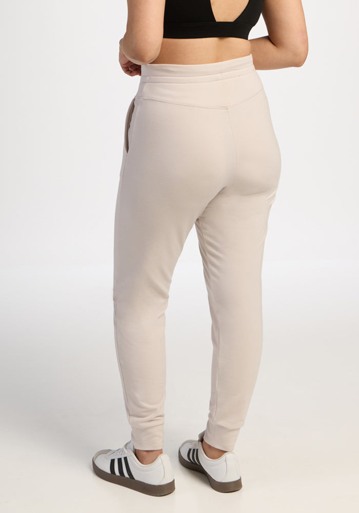 Person in Woolx Willa Joggers - Ecru, black crop top, and white Adidas sneakers against a white background.