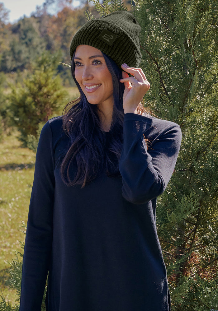 Woman in the Woolx Ria Chunky Beanie - Duffel Bag smiles outdoors in a long-sleeve shirt by greenery.