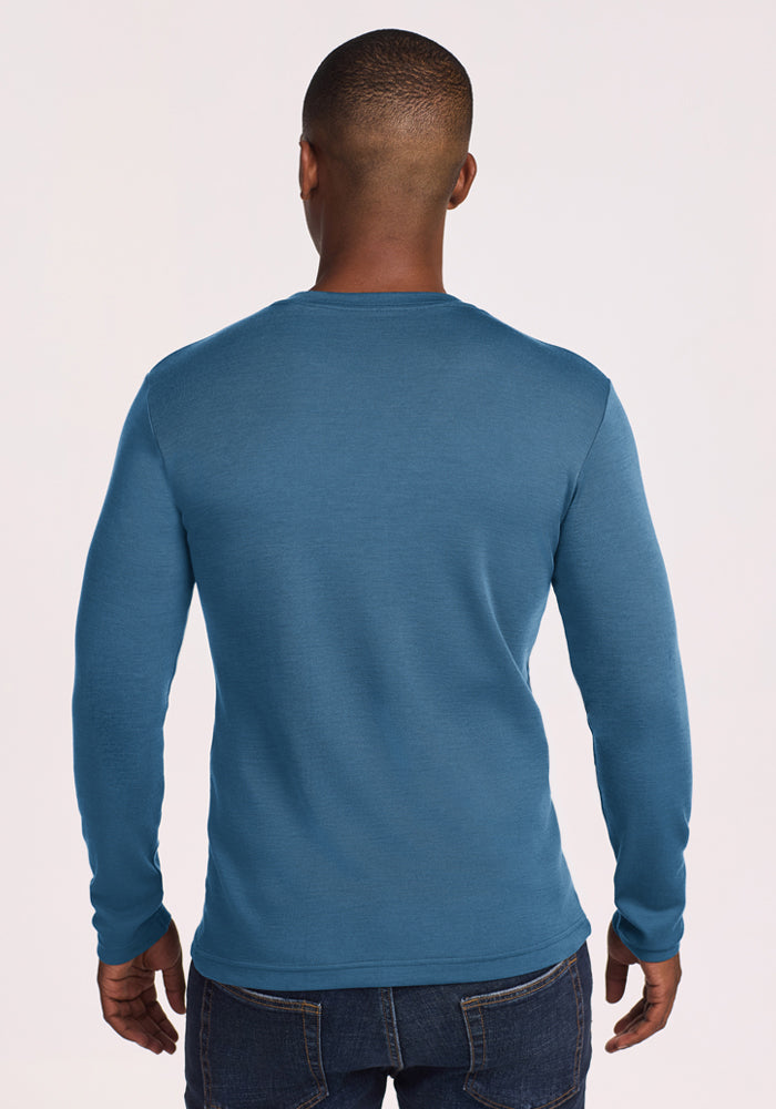 A man in a Woolx Easton Crew Neck Shirt - Blue Ashes and jeans, seen from behind, stands against a plain background.