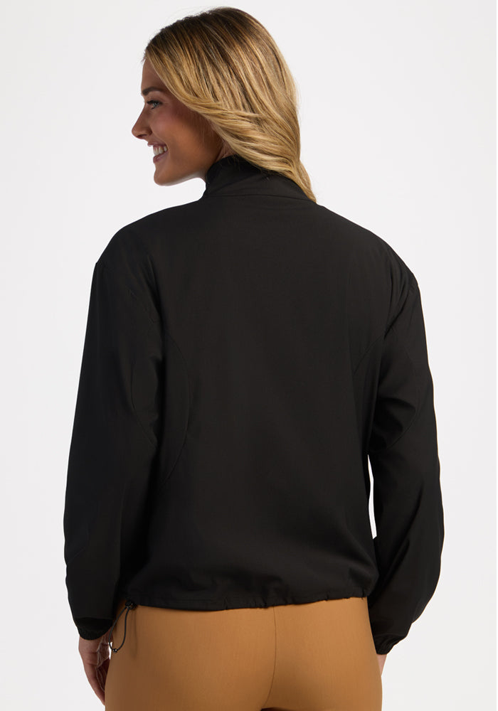 Woman facing away in Woolx Cooper Windbreaker - Black, zippered pockets, tan pants, smiling left.