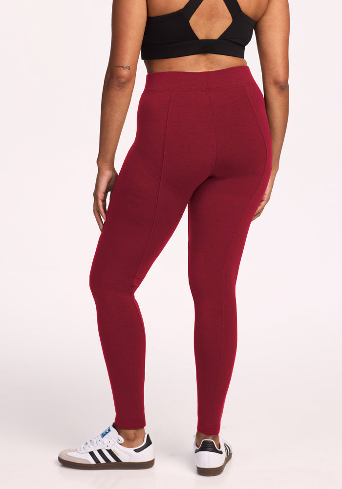 Woman in black sports bra, Woolx Stella Leggings - Pinot Noir, white Adidas sneakers, back to camera.