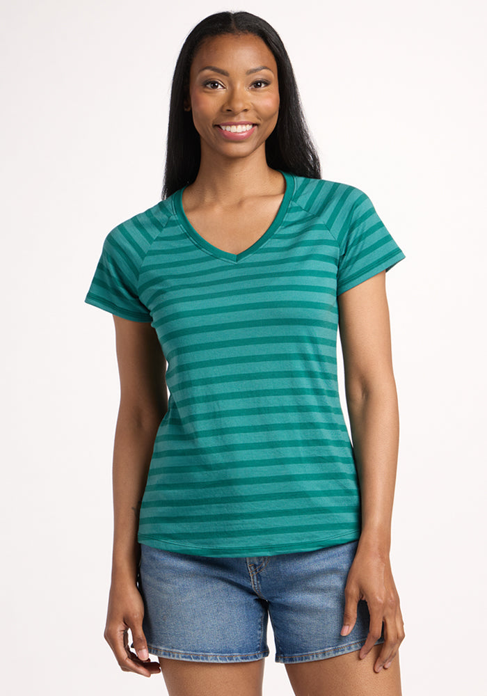 A woman with long dark hair, wearing the Woolx Mia V Neck - Woodland Stripe and denim shorts, smiles against a plain white background. 