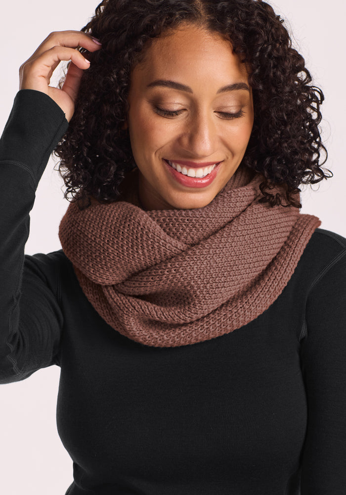 Smiling softly, a woman with curly hair wears the Woolx Noelle Infinity Scarf - Sable Heather—elegant and essential.