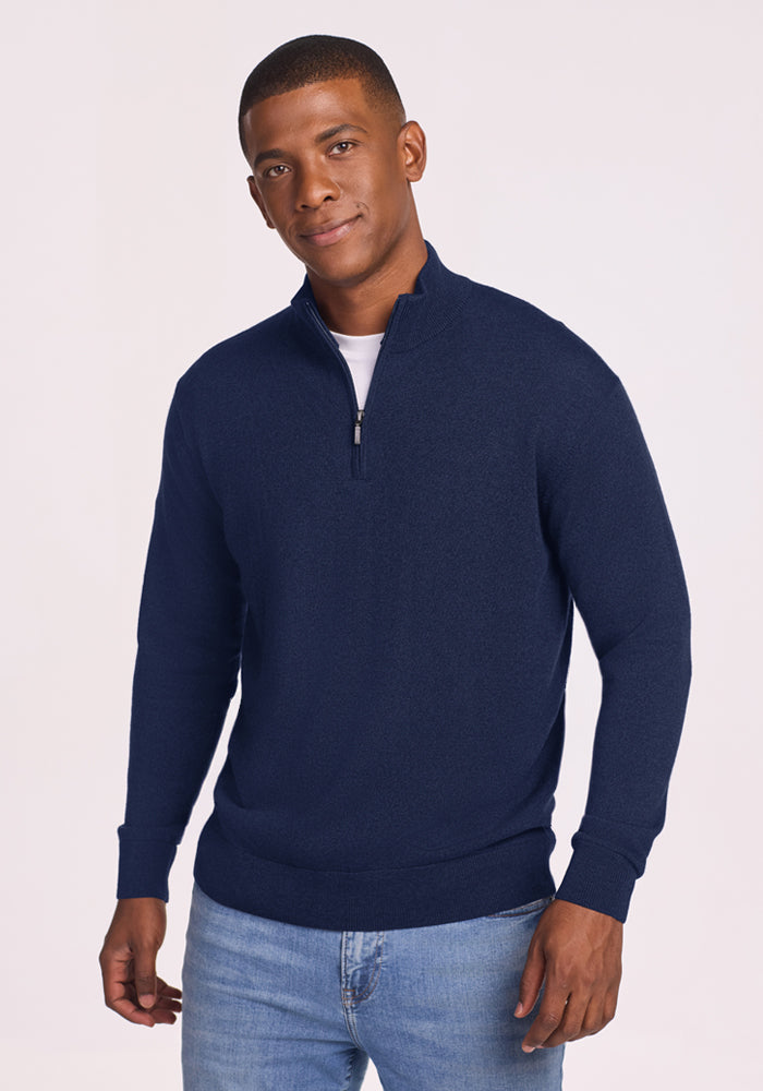 Man in a Woolx Enzo Quarter Zip - Ocean Cavern over a white shirt and jeans, stands against a light background. 