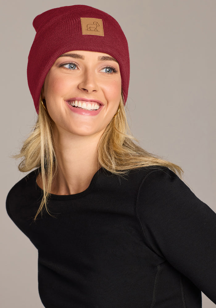 Smiling woman wearing the Woolx Baylor Beanie - Pinot Noir and black top, looking to the side against a plain backdrop.