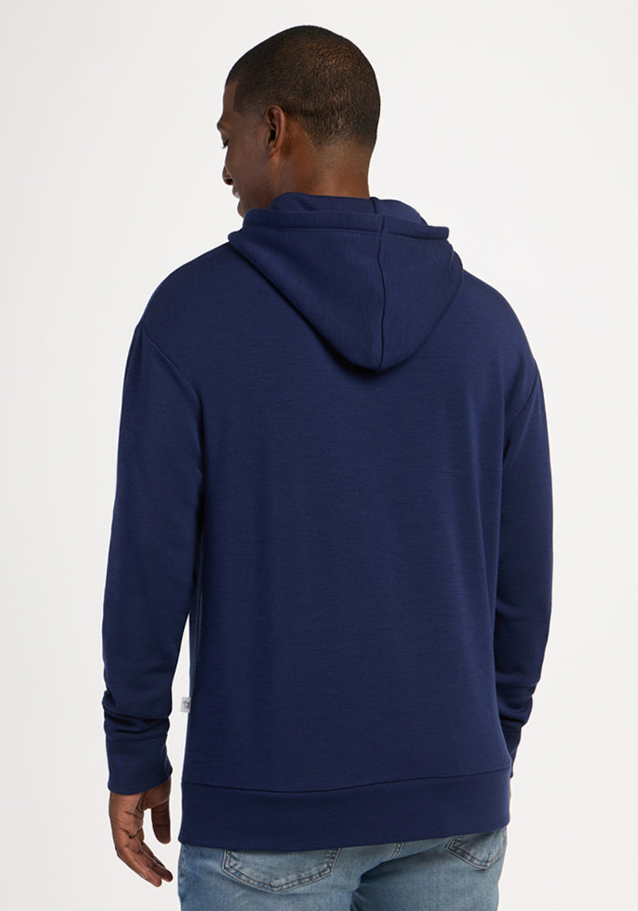 A man wears a Woolx Watson Pullover - Ocean Cavern hoodie and light blue jeans, facing away from the camera.