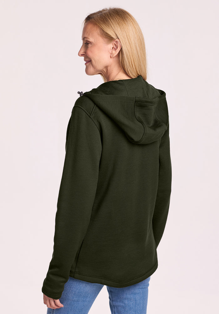 Blonde woman in Woolx Cubby Hooded Sweatshirt - Duffel Bag and jeans, hood up, stands against a light background.