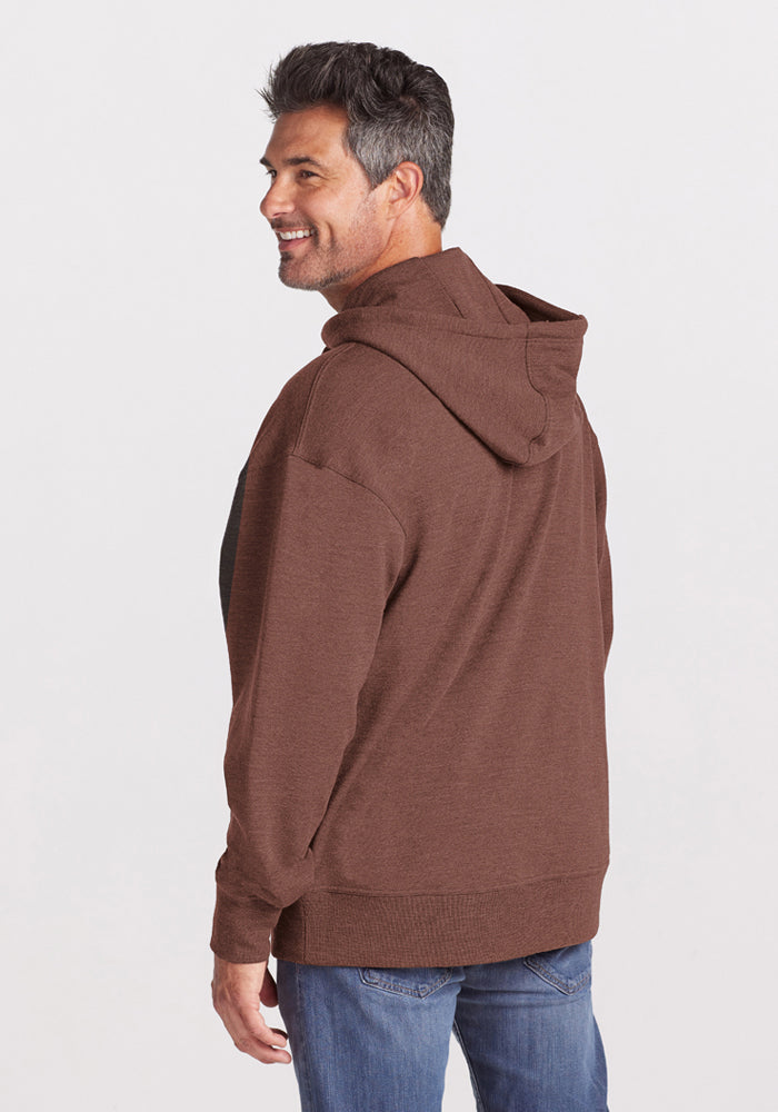 Man wears the Woolx Chase Hoodie in Sable Heather and jeans, smiling over his shoulder against a white backdrop.