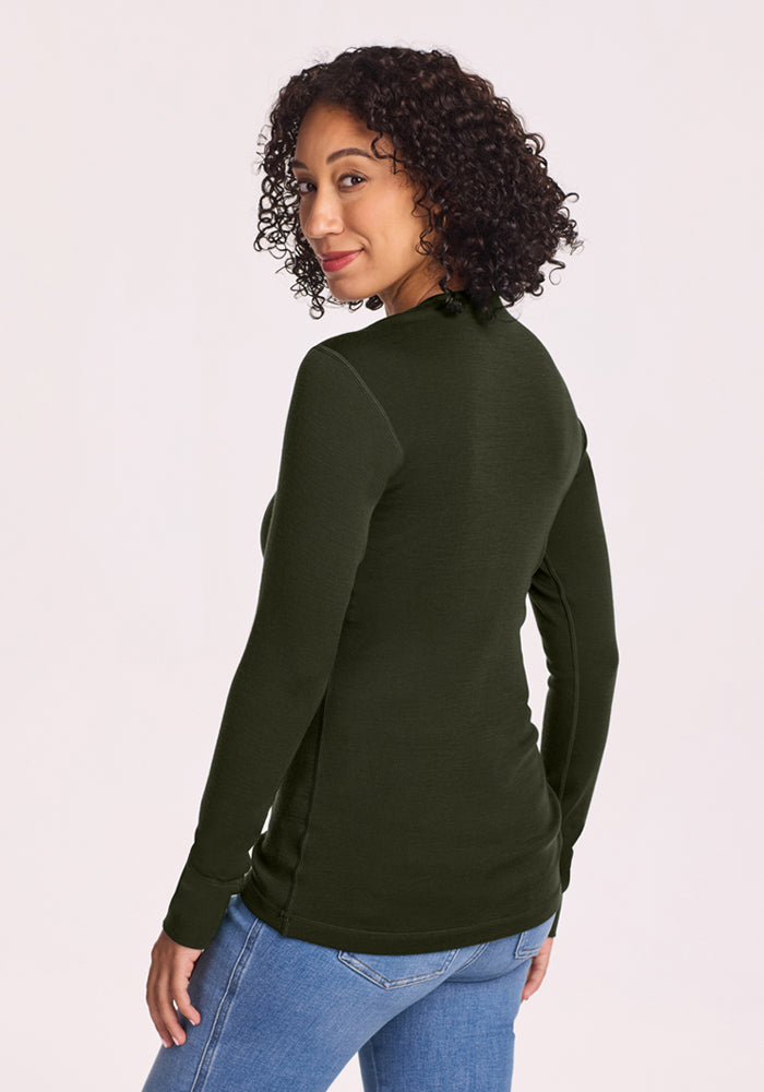 Woman with curly hair in the Woolx Hannah Long Sleeve Top - Duffel Bag, paired with jeans, smiling over her shoulder.