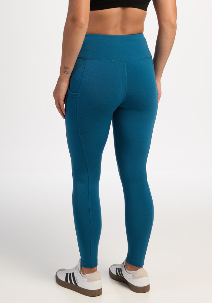 Model wears Woolx Piper Pocket Leggings - Blue Pine, black crop top, white sneakers; shown from the back on white.