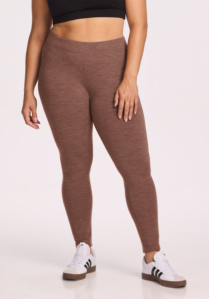 Woman wears Woolx Stella Leggings - Sable Heather, a black crop top, and white sneakers against a white background. 