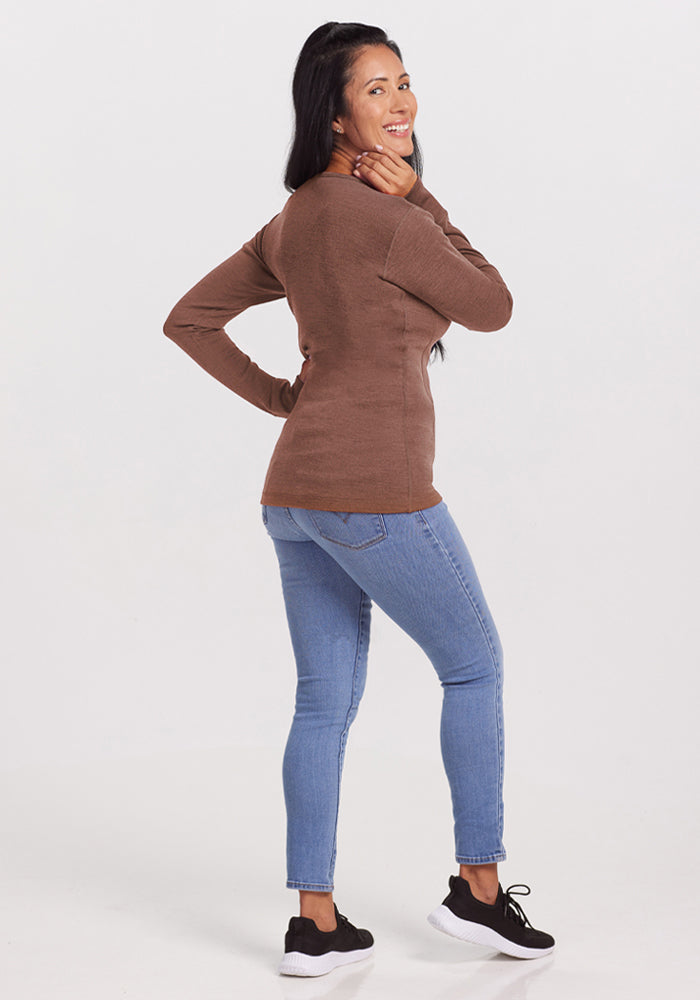 Smiling woman in Woolx Hannah Long Sleeve Top - Sable Heather and jeans looks over her shoulder, white background.