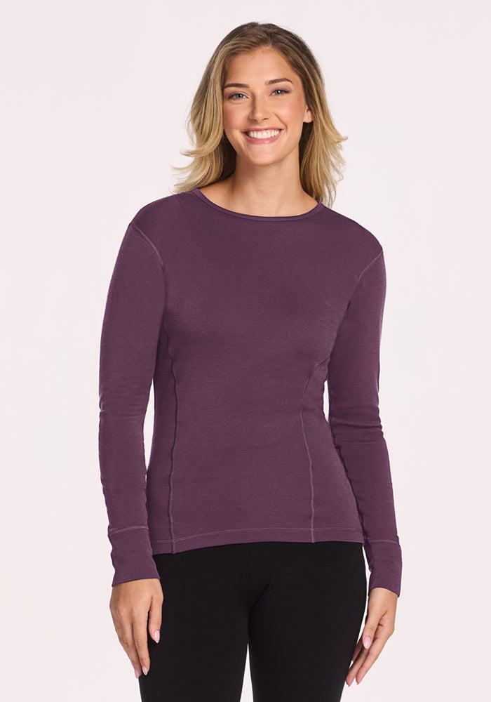 A woman smiles in a Woolx Hannah Long Sleeve Top - Purple Iris and black pants, against a plain light background. 