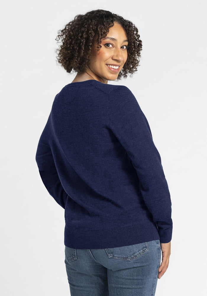 Woman with curly hair in the Woolx Francesca Sweater - Ocean Cavern, smiling over her shoulder at the camera.