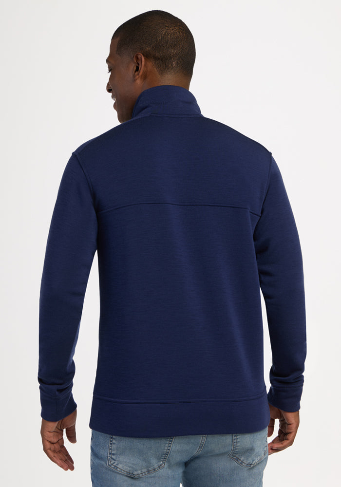 Man wearing Woolx Mason 1/4 Zip - Ocean Cavern and light blue jeans, facing away against a plain background.