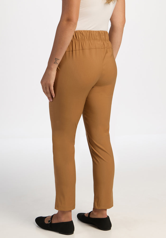 Woman wearing Woolx Nicole Tall Ankle Pant in Saddleback, white top, black shoes, back to camera on plain background.