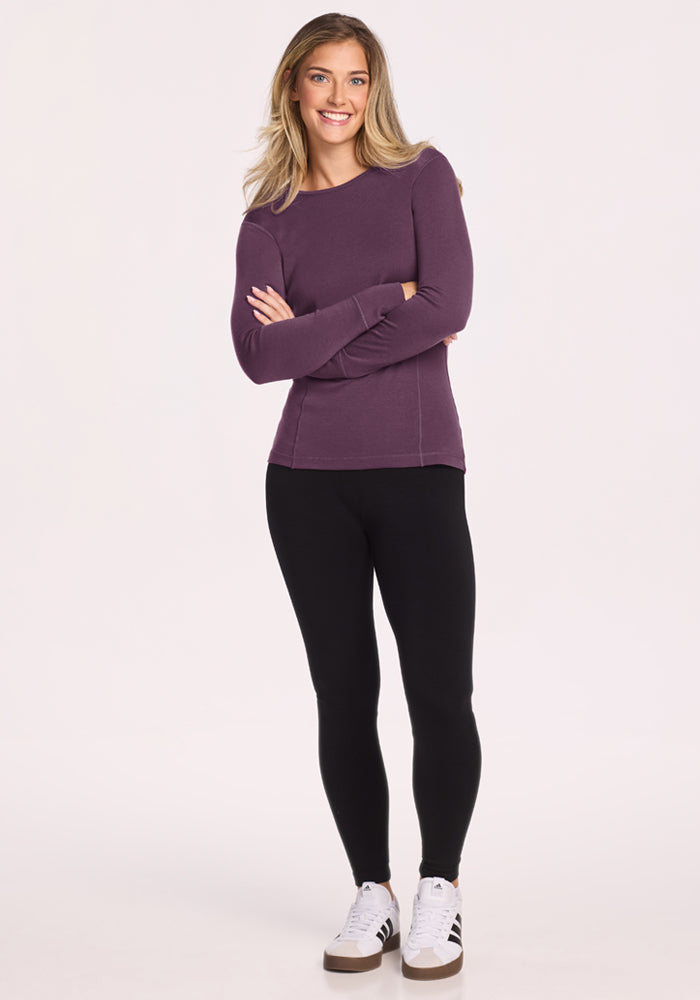 Woman in a Woolx Hannah Long Sleeve Top - Purple Iris, black leggings, and sneakers stands smiling with arms crossed.