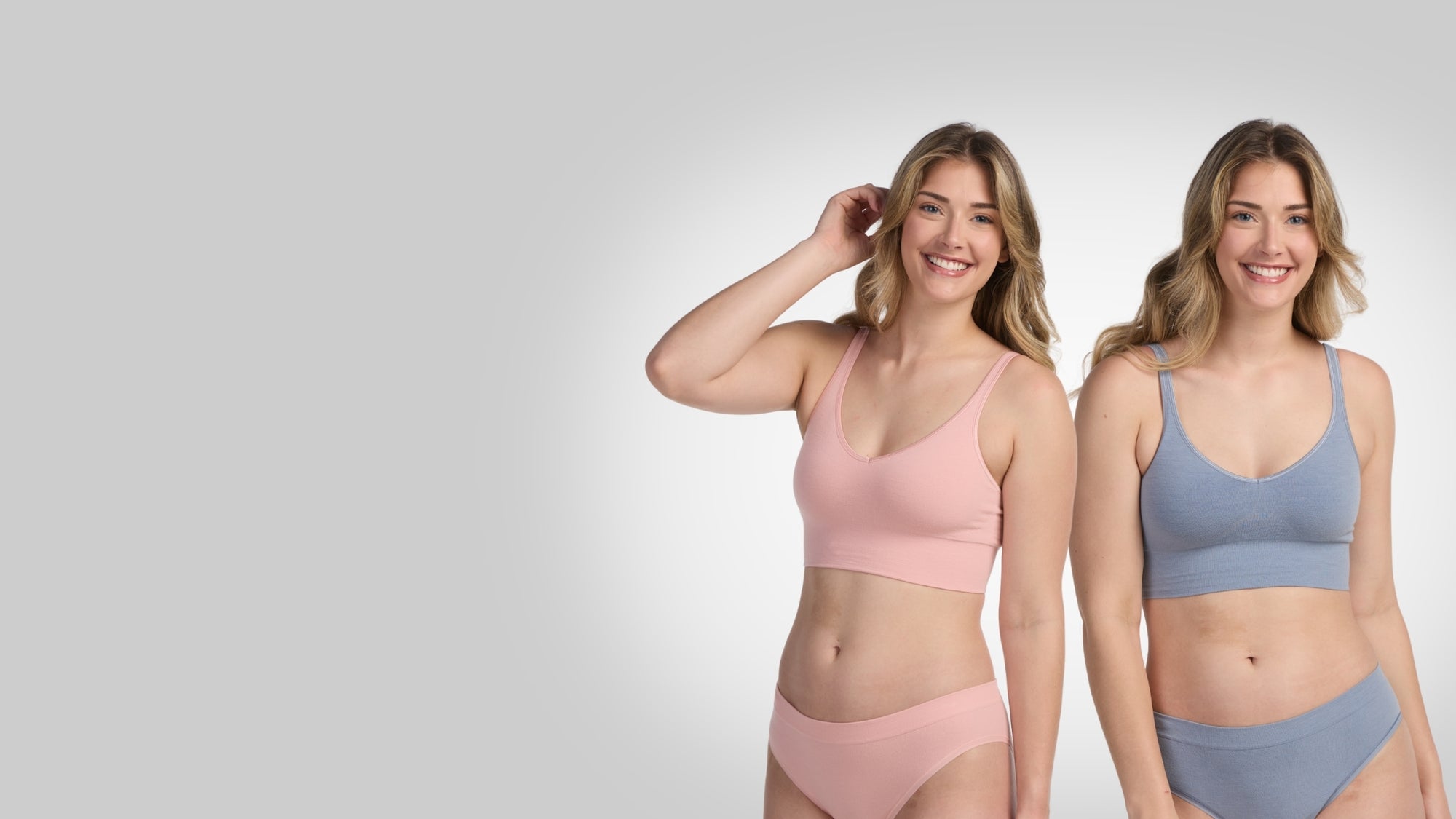 Two women wearing pink and blue sports bras with matching underwear on a light gray background