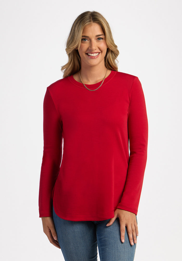 Smiling woman with long blonde hair wears the Woolx Blair Tunic in Maraschino Cherry and blue jeans, against white. 
