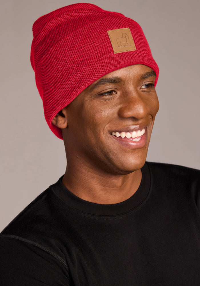 Smiling man in a Woolx Baylor Beanie - Maraschino Cherry with brown patch and black shirt, neutral background.
