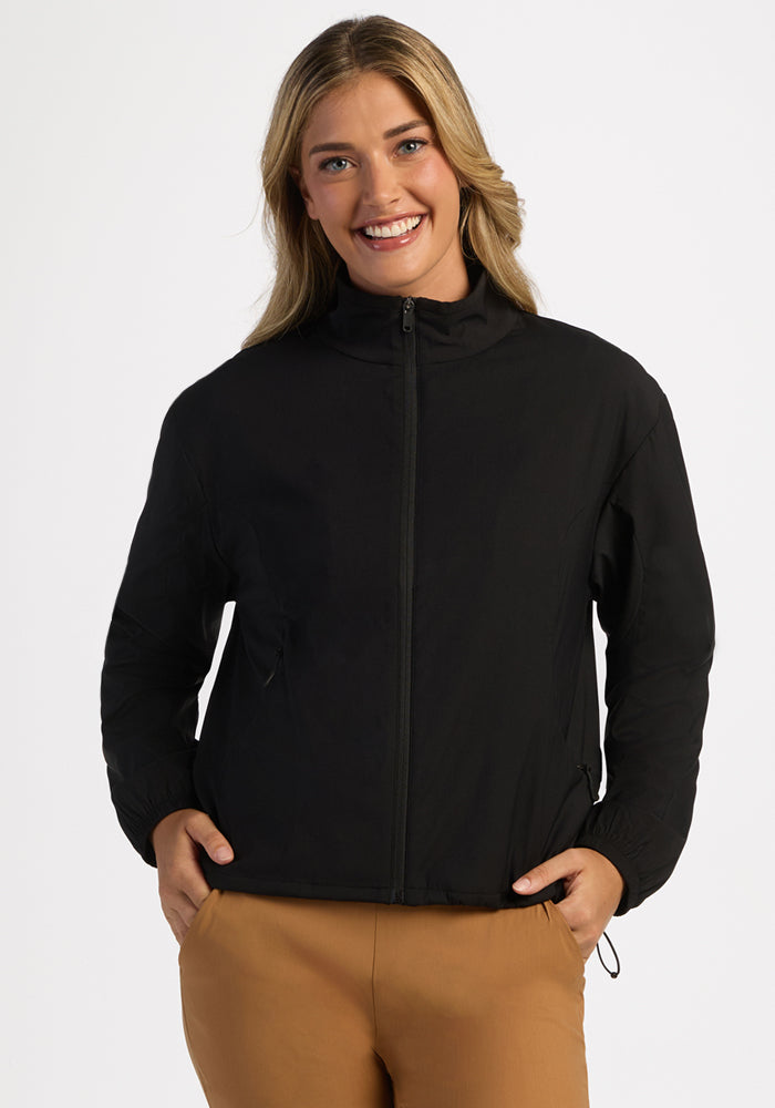 Person smiling in Woolx Cooper Windbreaker - Black, with zip pockets and tan pants, against a plain white background. 