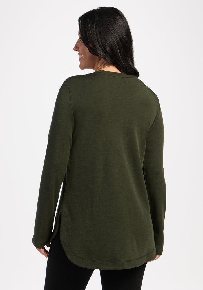 Woman facing away in a Woolx Blair Tunic - Duffel Bag, odor-resistant Merino wool, with black pants on white background.
