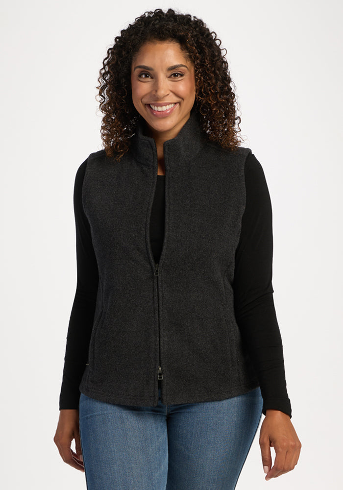 Smiling woman wears Woolx Haley Vest - Carbon Black over a black shirt and jeans, standing against a white backdrop. 