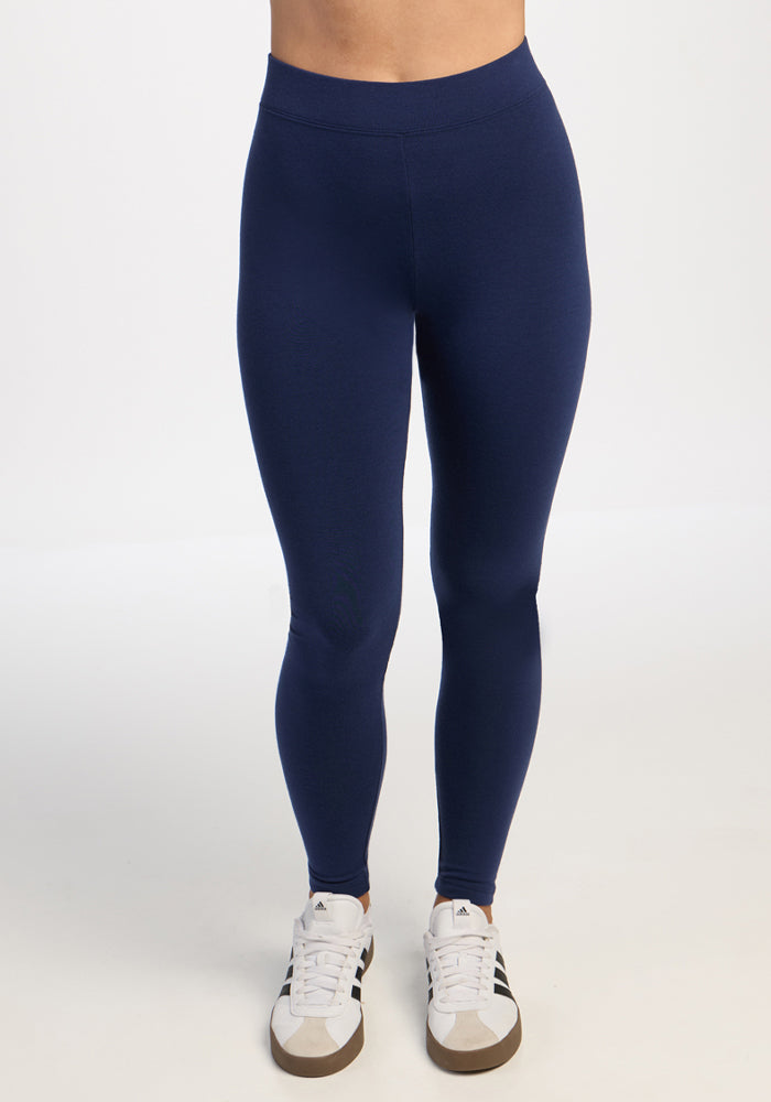 Model wears Woolx Stella Leggings in Ocean Cavern and white sneakers with black stripes, standing on a white background. 