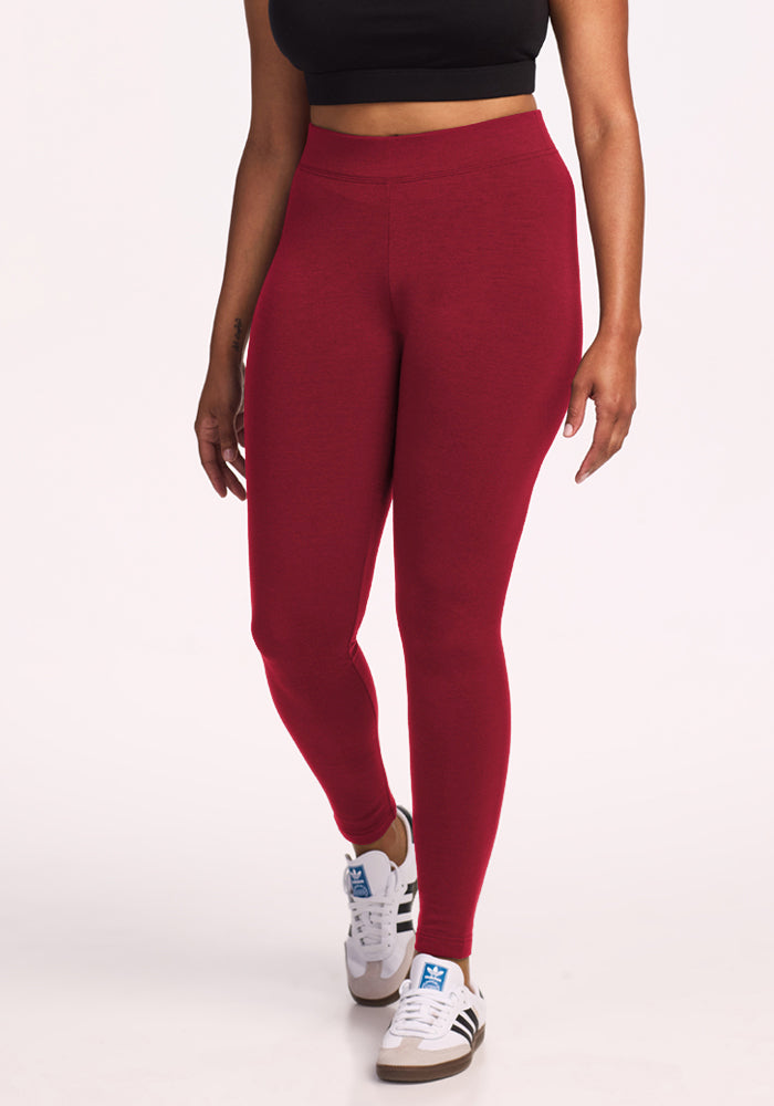 Person wears Woolx Stella Leggings in Pinot Noir, a black crop top, and white sneakers against a plain white background. 