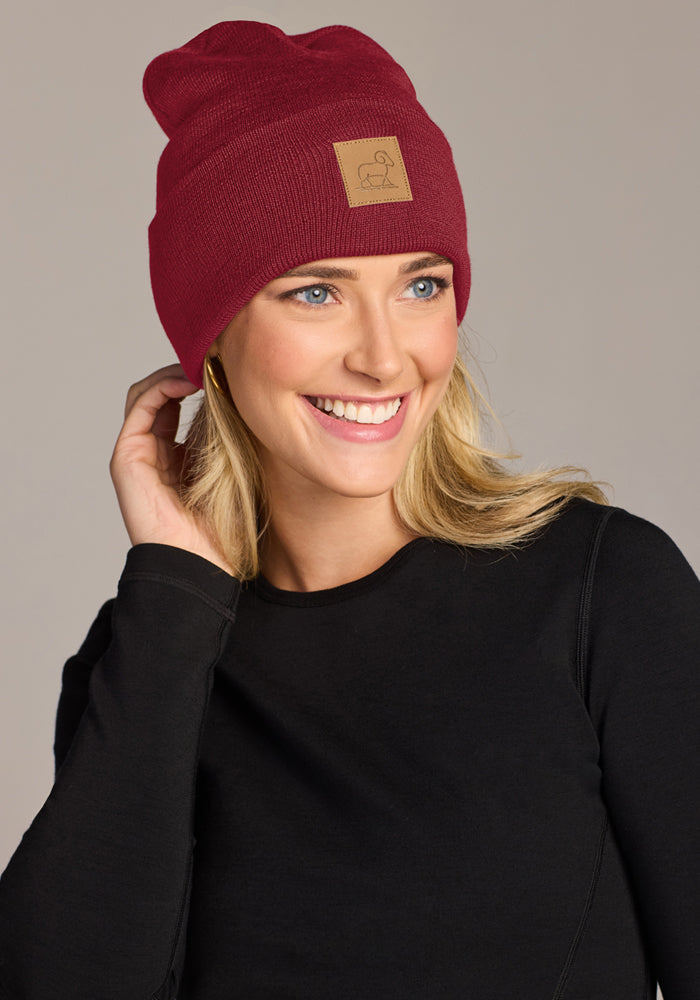 Smiling woman in a Woolx Baylor Beanie - Pinot Noir and black shirt, touching her head, looking slightly left.