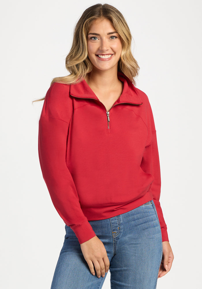 A woman wears a bright red Woolx Tori 1/4 Zip - Maraschino Cherry merino wool sweater and blue jeans. | Ariana is 5'11", wearing a size S