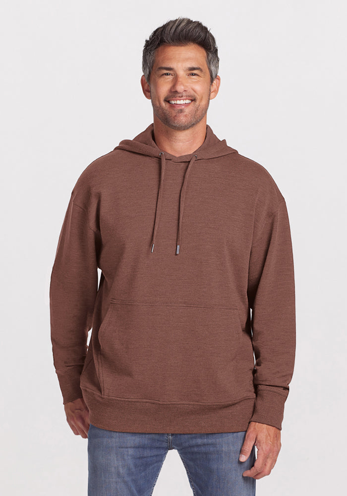 Smiling man wears the Woolx Chase Hoodie in Sable Heather and blue jeans, standing against a plain light background. | Matthew is 6’, wearing a size L