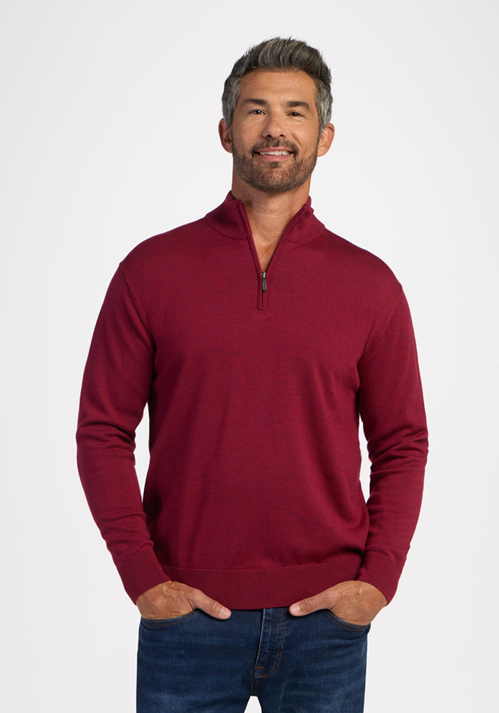 Man wears the Woolx Enzo Quarter Zip in Beet Red, smiling with hands in pockets against a white background. 