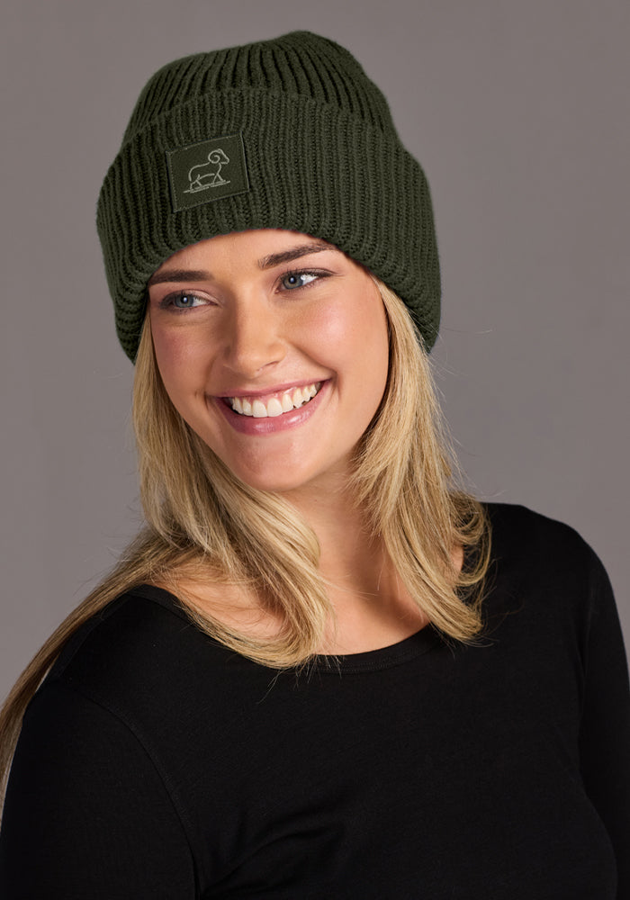 Smiling woman in Woolx Ria Chunky Beanie - Duffel Bag, black shirt, right-facing on gray; classic winter style.