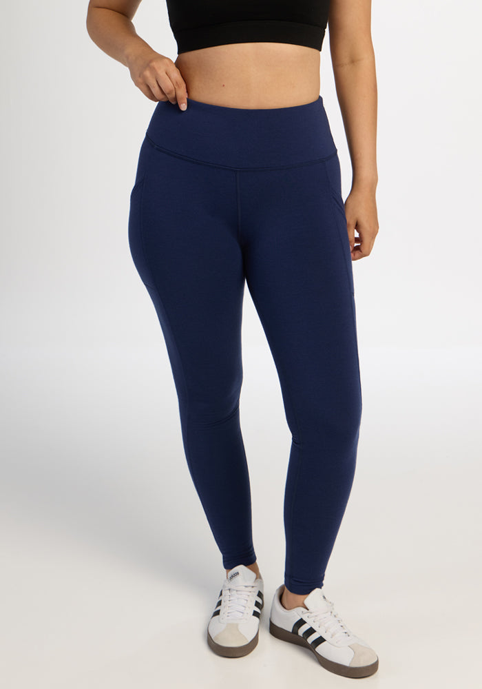 Person wears a black crop top, Woolx Piper Pocket Leggings - Ocean Cavern, and white sneakers against a plain background. 