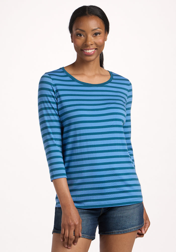 Smiling woman with long hair wearing the Woolx Jenny 3/4 Sleeve Crew Neck in Coastal Stripe and denim shorts, standing against a plain light background. 