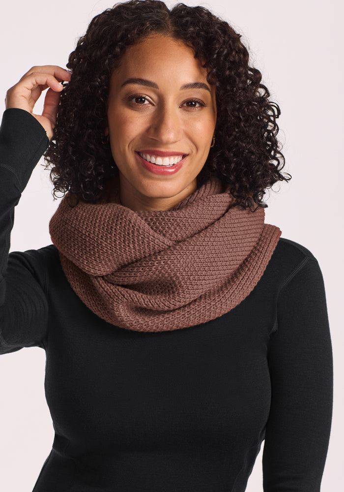 Smiling woman with curly hair wears Woolx Noelle Infinity Scarf - Sable Heather, perfect for your winter wardrobe.