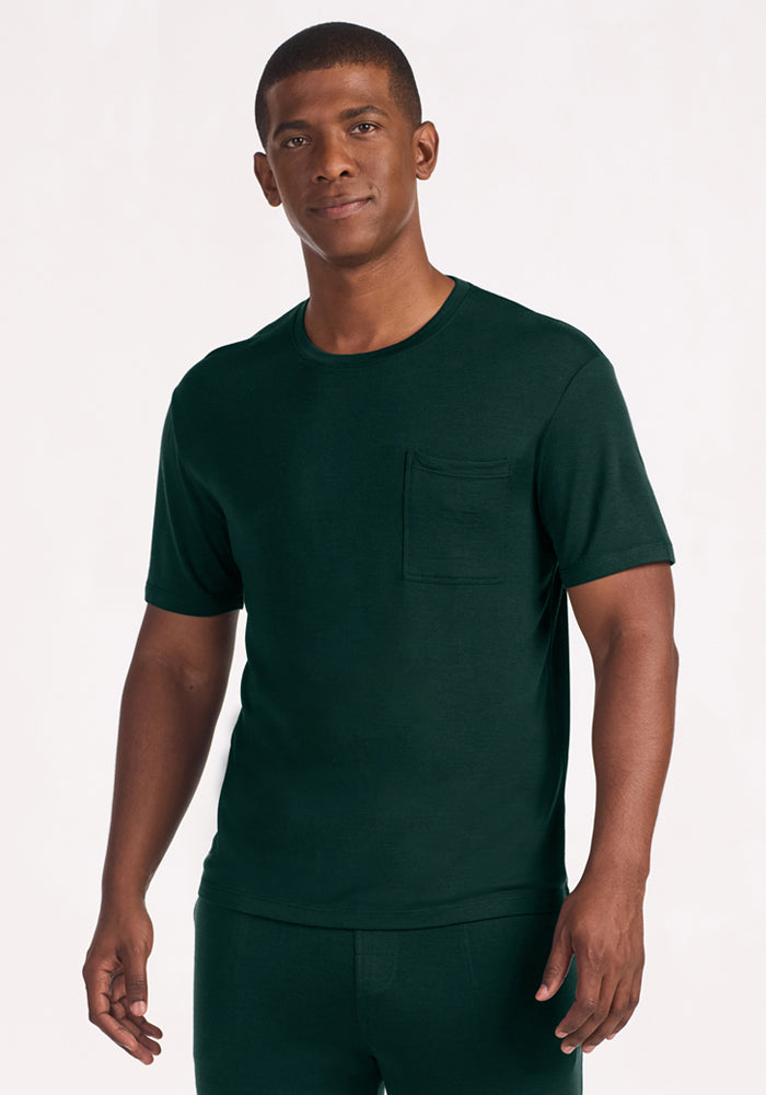 A man wearing a dark green Woolx Finn Top - Deep Pine merino wool short-sleeved crew neck t-shirt with a chest pocket. 
