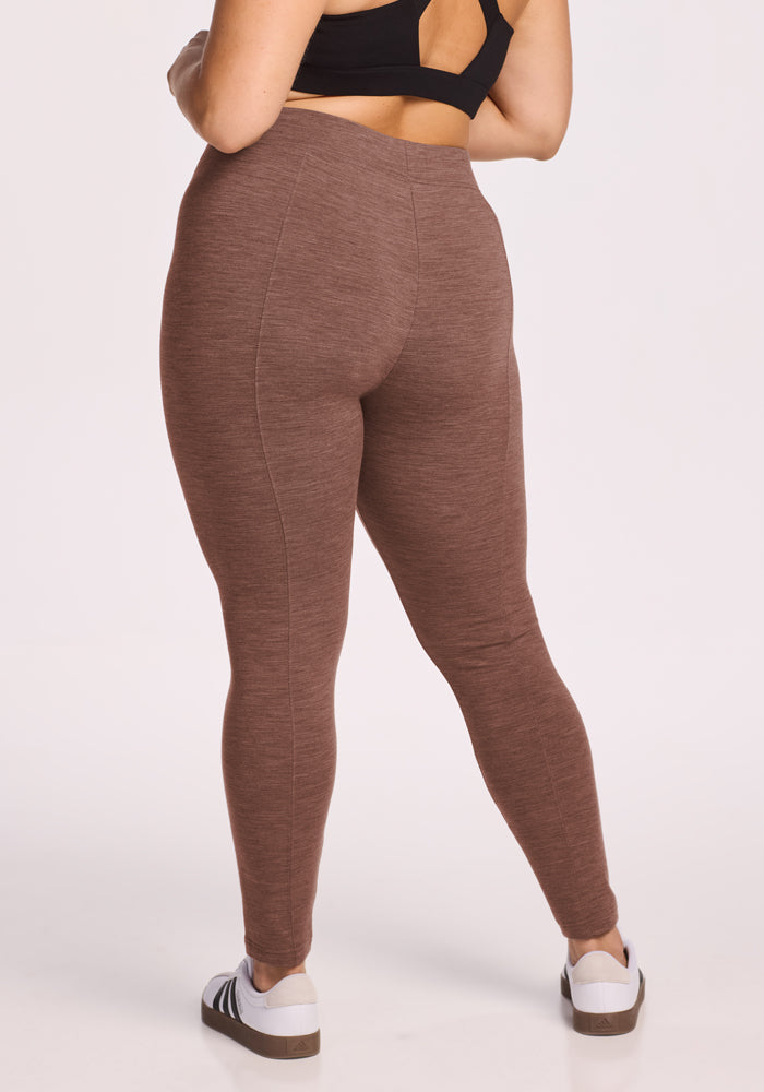 Woman wears Woolx Stella Leggings in Sable Heather, black sports bra, and white sneakers; shown from the back.
