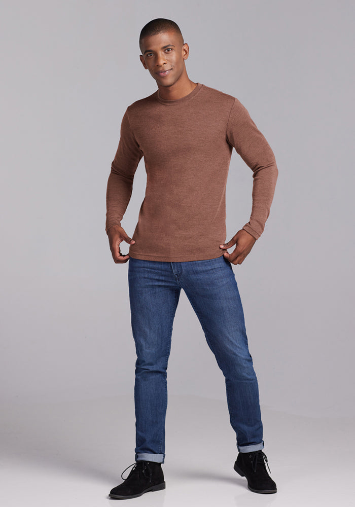 Man in a Woolx Easton Crew Neck Shirt - Sable Heather and blue jeans poses against a plain light gray background.
