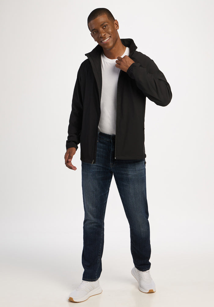 Man wears Woolx Dominator Windbreaker - Black with zippered pockets, jeans, and white shirt against a plain background.