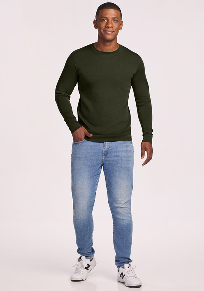 Man in a Woolx Explorer Base Layer - Duffel Bag, blue jeans, and white sneakers smiles against a plain background.