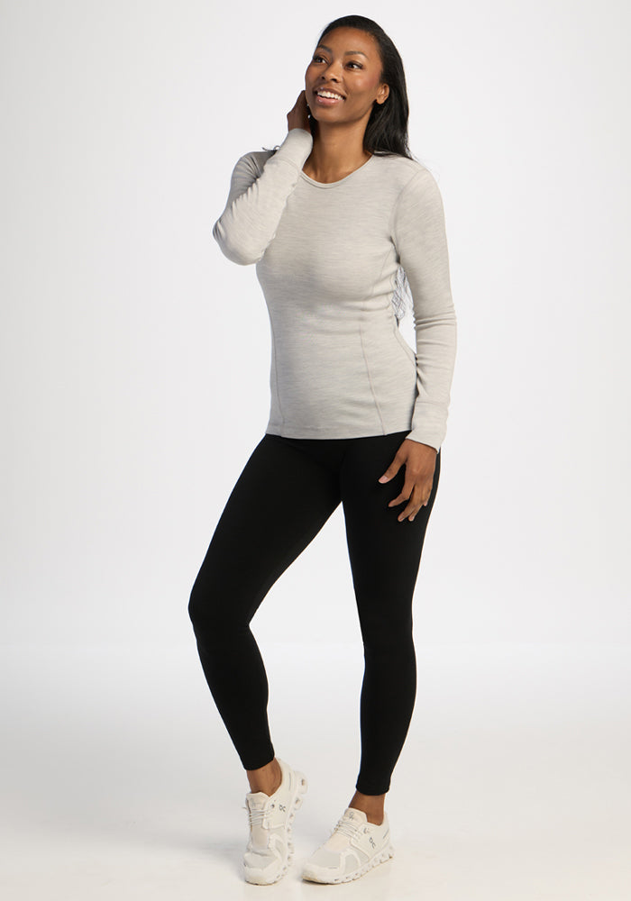 Smiling woman in Woolx Hannah Long Sleeve Top - Light Ash, black leggings, and white sneakers.