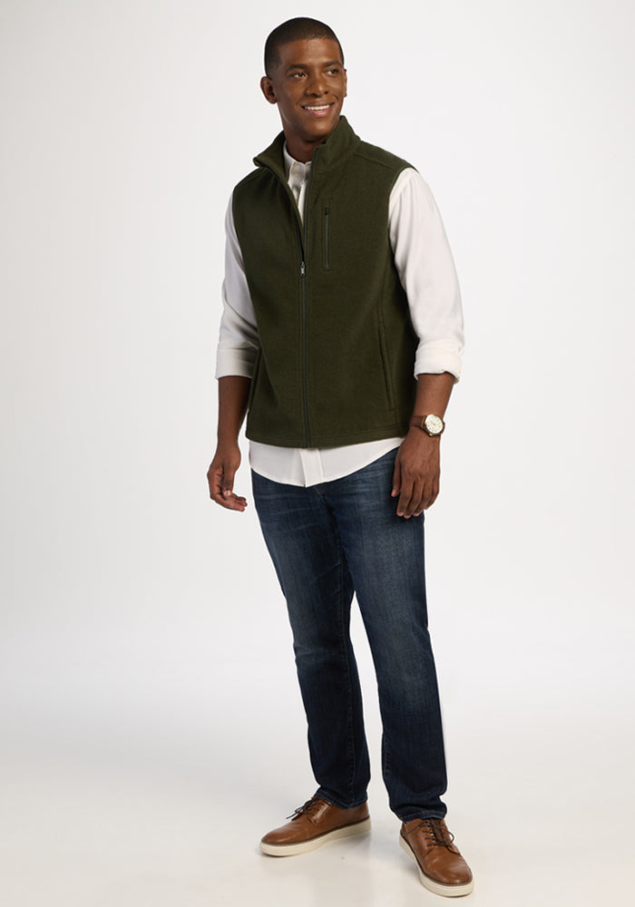 A man wearing an olive green Woolx Everest Vest - Duffel Bag over a white button-down shirt and blue jeans.